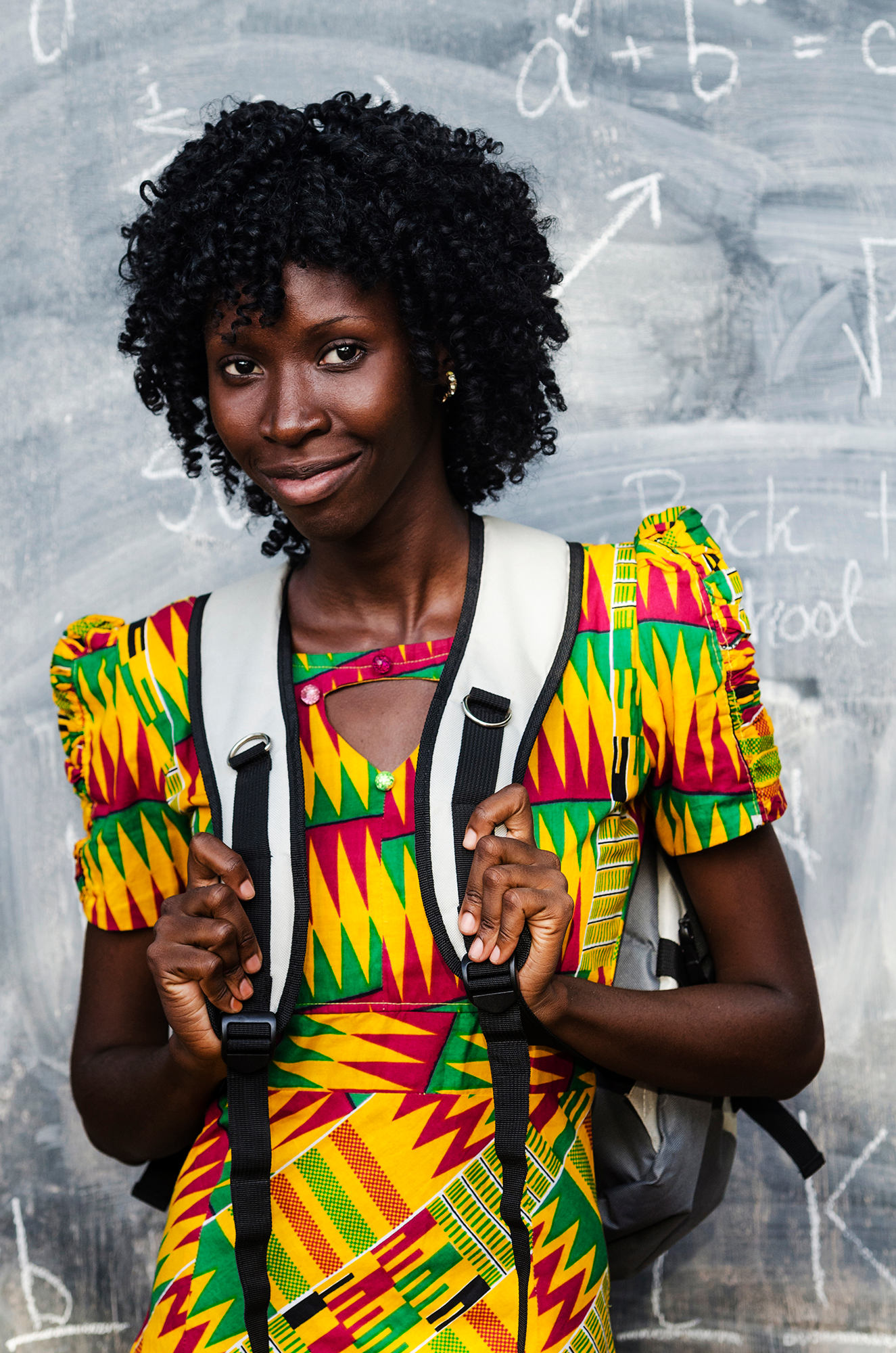 An African woman proudly holding an university bag in front of a school blackboard.