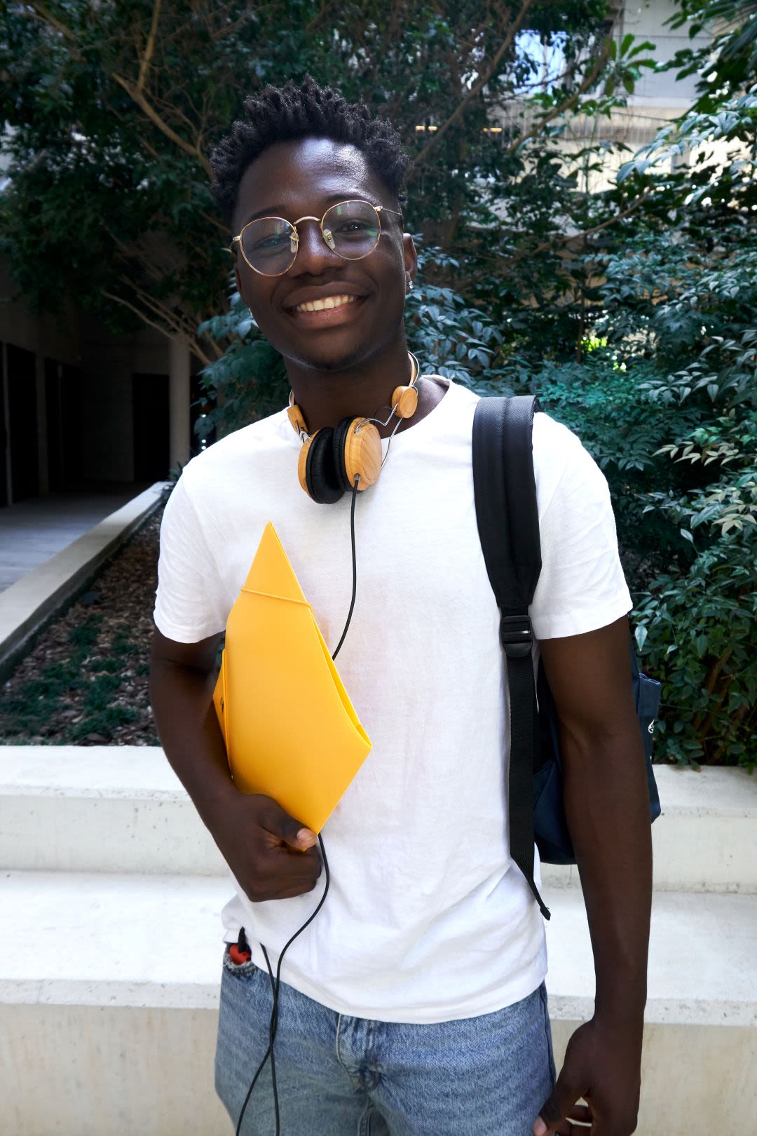 Cheerful African student looking camera confident while standing at school patio. Vertical portrait of young man at university campus.