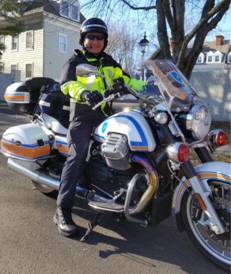 Mr. Bill Min in his EMT uniform sitting on a Westport Emergency Medical Services motorcycle.