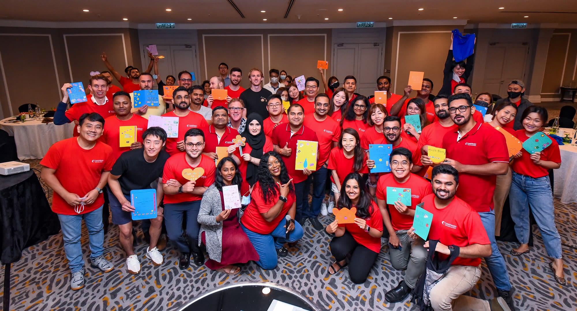 A group of approximately 30 Risk employees posing for a volunteer photo holding handmade children cards.