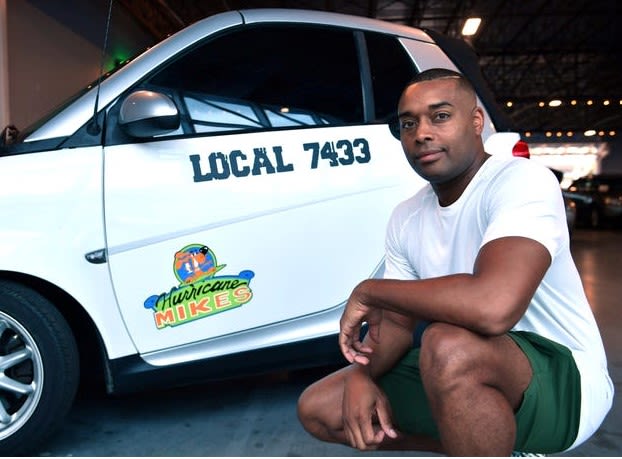 Javon Chapman kneeling next to the SmartCar he pushed for miles to raise money for The Special Olympics.